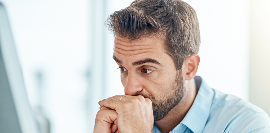 A white man in a dress shirt holding his hands to his chin. He looks worried.