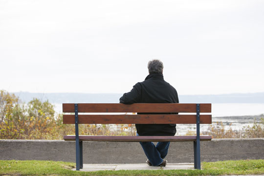 Seen from behind, a man sits alone on a bench looking at the sea