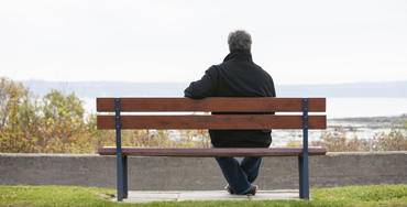 Seen from behind, a man sits alone on a bench looking at the sea