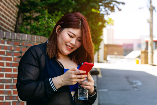 A Korean woman smiles as she reads a message on her phone