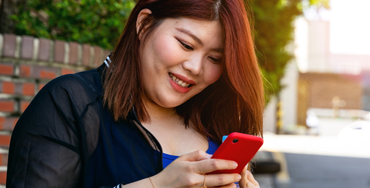 A Korean woman smiles as she reads a message on her phone
