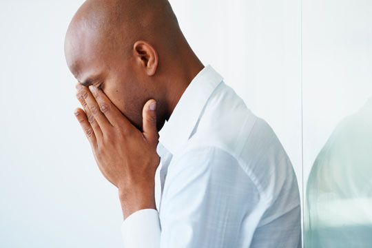 A black man in a dress shirt with his head in his hands