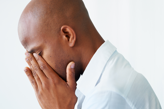 A black man in a dress shirt with his head in his hands