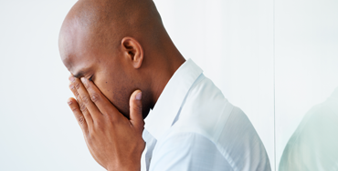 A black man in a dress shirt with his head in his hands